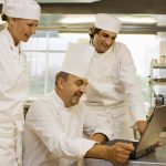 Three chefs looking at a laptop